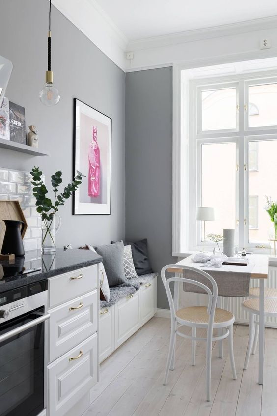 Beyaz Shaker tarzi dolaplari gri tezgahlari gri duvarlari ve kucuk bir yemek alani bulunan bir Iskandinav mutfagi