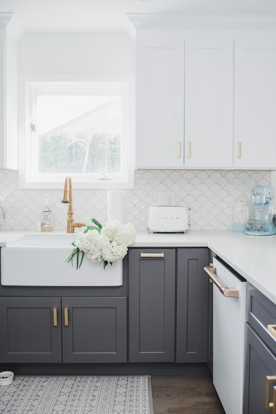 Beyaz ust dolaplar ve alt gri dolaplar altin ve pirinc kulplar ile modern bir mutfak beyaz balik pulu desenli arka zemin ile tamamlanmistir