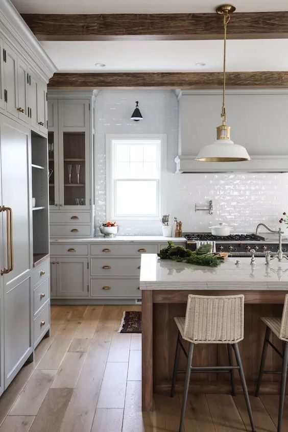 Guvercin gri dolaplar beyaz fayans arka zemini beyaz lambalar ve ahsap kirisler ile birlikte bir mutfak adasi bulunan vintage tarzda bir mutfak
