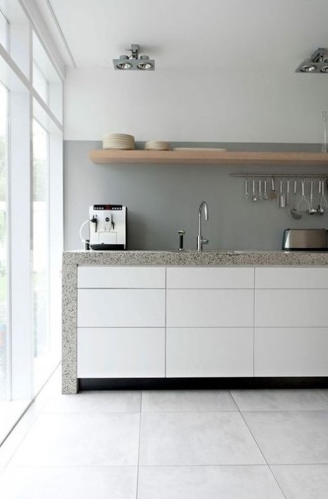  Pürüzsüz beyaz dolaplar, beton arka plan ve gri taş tezgahlar ile şık minimalist bir mutfak, artı bir ahşap raf.