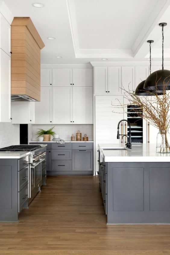 Ust kisimda beyaz alt kisimda koyu gri dolaplar beyaz tezgahlar ve arka plan siyah sarkit lambalar ile modern bir ciftlik evi mutfagi