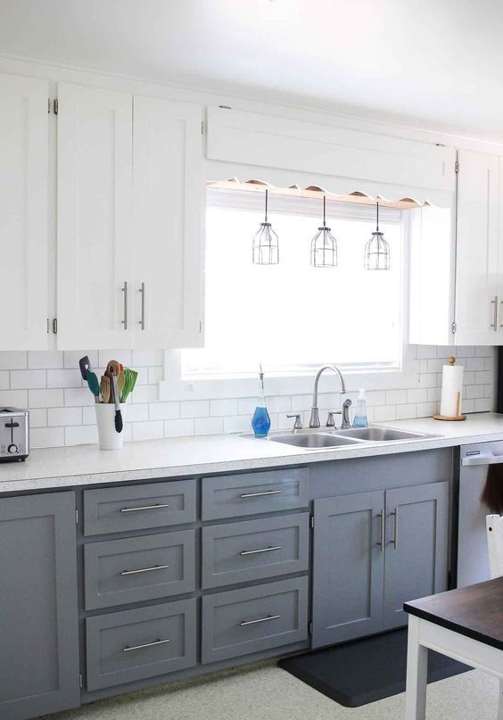 Ust kisimda beyaz dolaplar alt kisimda gri dolaplar sarkit lambalar ve bazi noktalarda metalik dokunuslar bulunan modern bir ciftlik tarzi mutfak